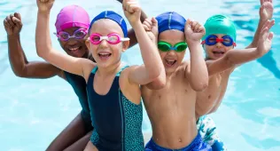 Four children with their arms in the air at the pool