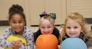 three small girls, laying on their stomachs and holding dodgeballs